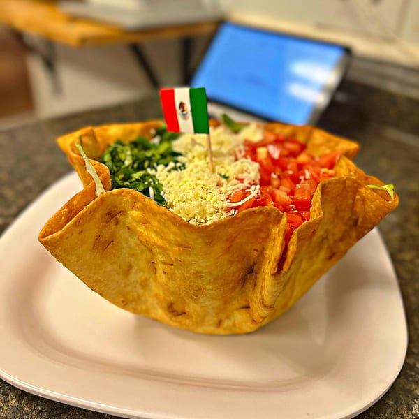 A taco salad in a crispy fried tortilla bowl, topped with a small Mexican flag.