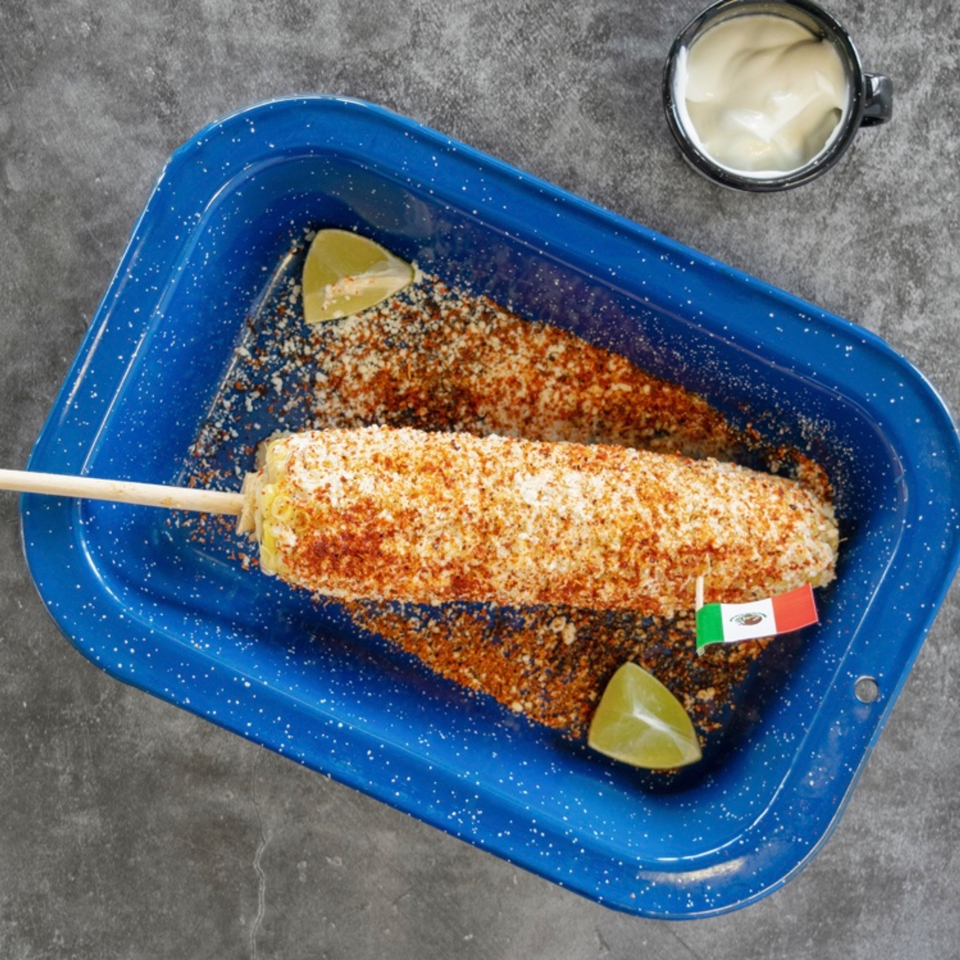 Elote, Mexican street corn, on a stick with chili powder and cheese, served in a blue tray.